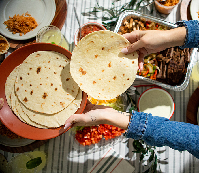 Fresh plate of tortillas being handed to someone. On the table under there are various plates of Chuy's food.