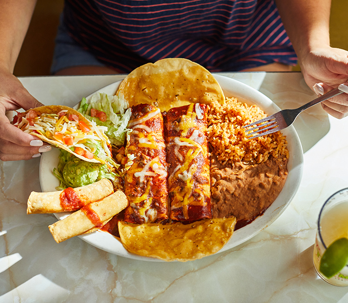 Big plate of Chuy's food featuring flautas, chimichangas, Mexican rice, beans, guacamole, and a taco. Margarita served on the side.