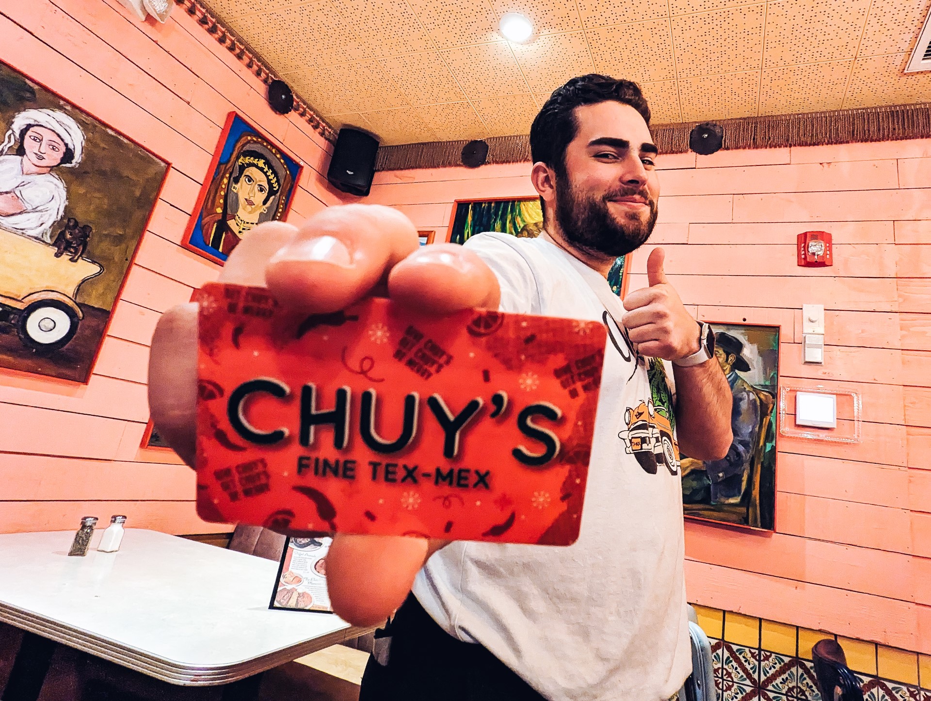 Guy holding up a Chuy's gift card at a Chuy's restaurant location.