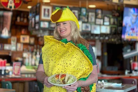 Guest wearing a taco costume and holding tacos at Chuy's restaurant during the National Taco Day celebration.