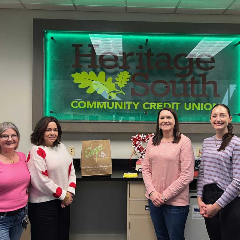 Four women standing next to a Chuy's bag under the Heritage South Community Credit Union sign.