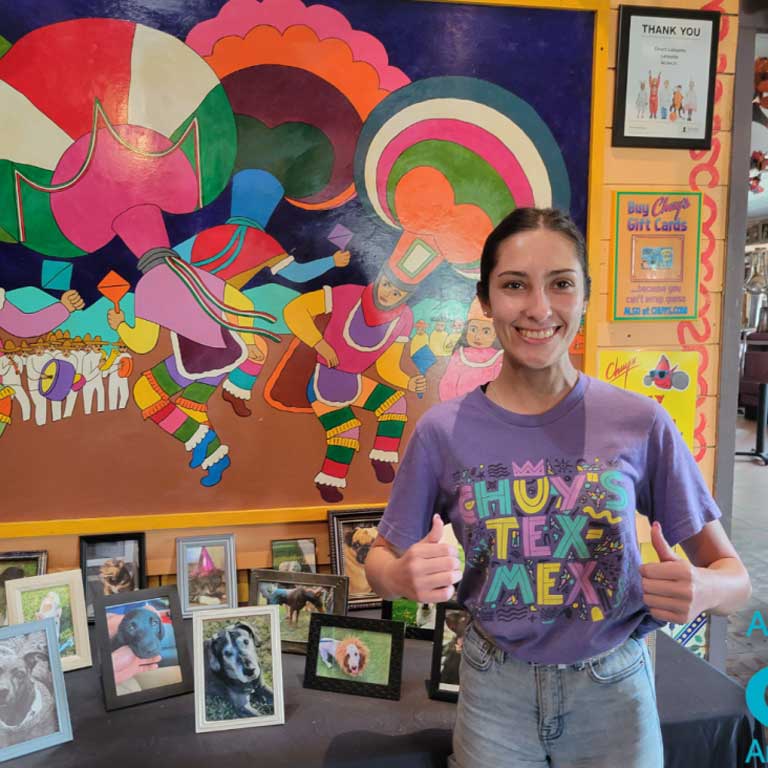 Woman giving a thumbs up next to the Chuy's pet adoption table, which features pictures of animals.