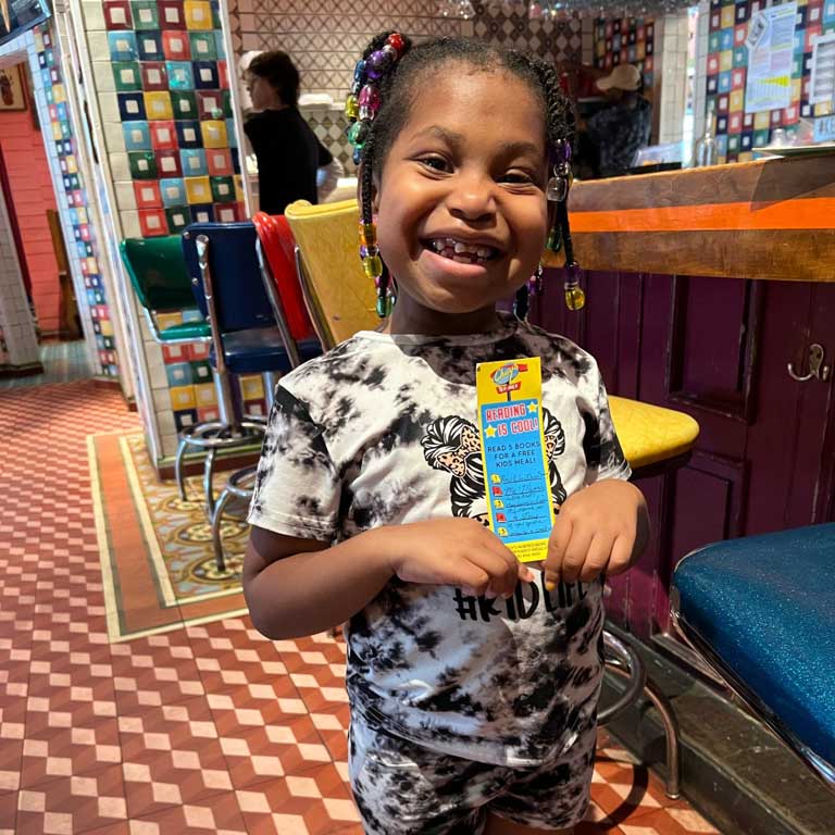 Girl smiling holding a Chuy's 'Reading is Cool!' bookmark.