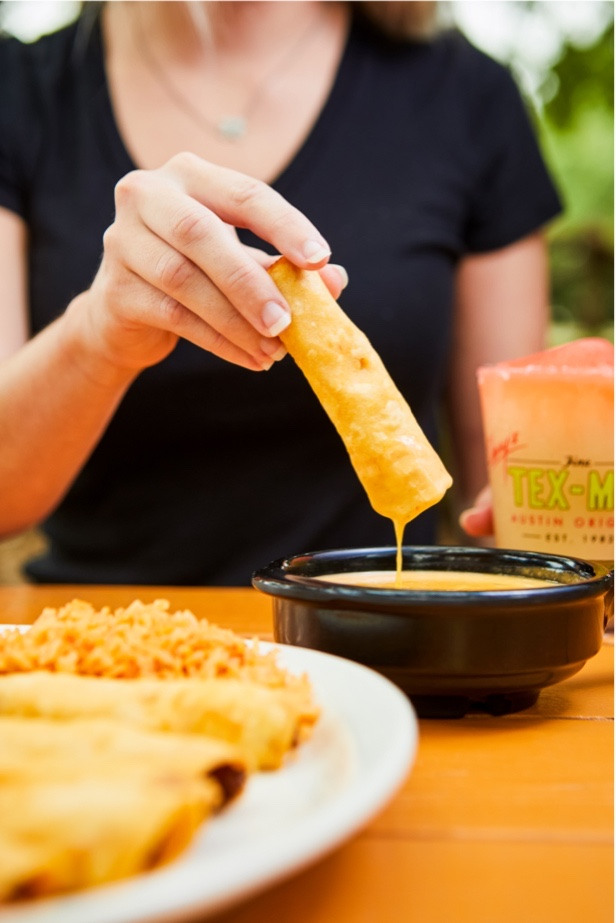 Chuy's Flauta dipped in Queso, next to a drink and Mexican rice.